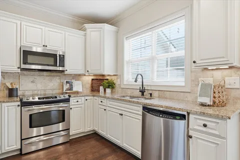 a kitchen with granite countertop white cabinets white stainless steel appliances a sink and a window