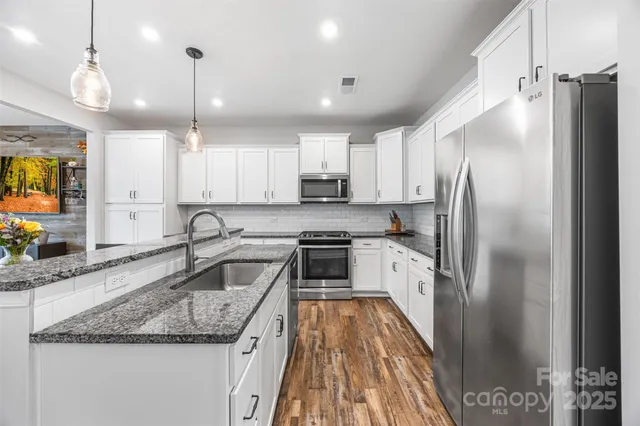 a kitchen with stainless steel appliances granite countertop a kitchen island a stove and a wooden floors