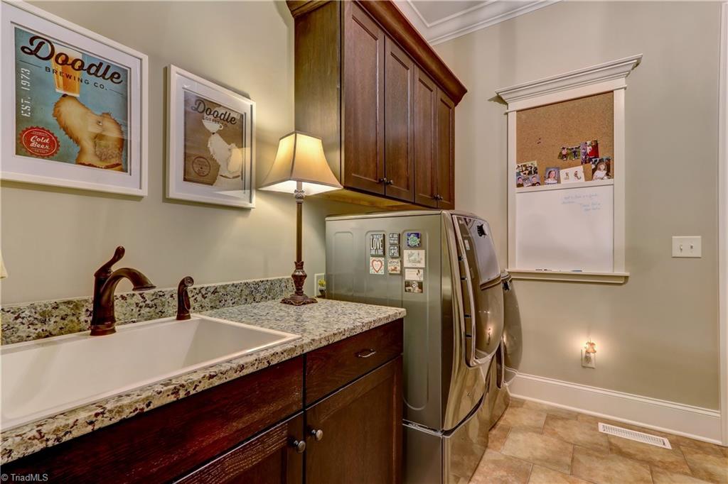 6865 Matzinger Court Oak Ridge, NC 27310 - Photo 17 of 28 The laundry room has a tile floor, large sink, granite counter top, and plenty of storage. Not shown in this view is a built in bench with bead board wall detail and cubby storage with 5 hooks.