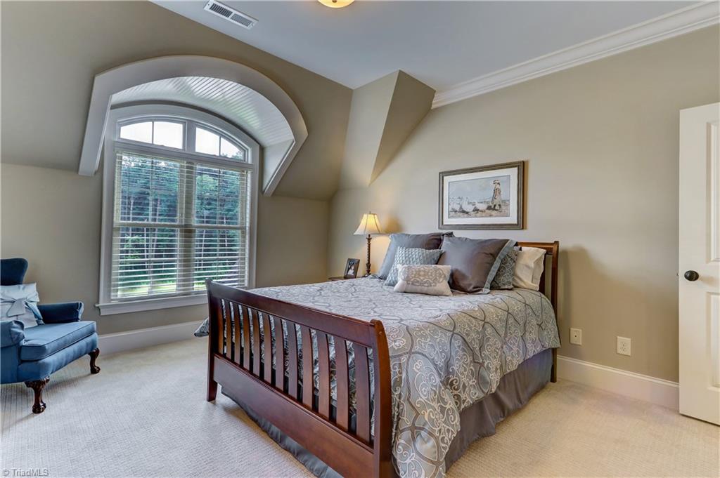 6865 Matzinger Court Oak Ridge, NC 27310 - Photo 18 of 28 Bedroom 2 - architectural details continue in the barrel ceiling detail above the window. Walk-in Closet, wall to wall carpeting, ceiling light, base and crown molding, and wood blinds. Shared Jack and Jill bath.