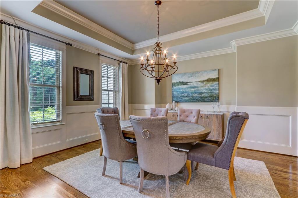 6865 Matzinger Court Oak Ridge, NC 27310 - Photo 2 of 28 The Dining Room features hardwood flooring, wainscoting, crown molding, stepped up tray ceiling, and central chandelier.