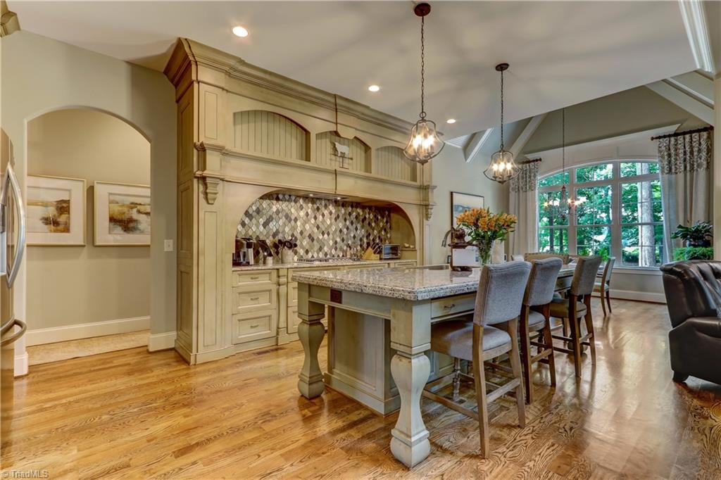 6865 Matzinger Court Oak Ridge, NC 27310 - Photo 8 of 28 This kitchen will make all cooks happy. Shown here, granite counter tops, large island with sink, recessed and pendant lighting, and 5-burner gas stove set in a large alcove with full height decorative tile backsplash.