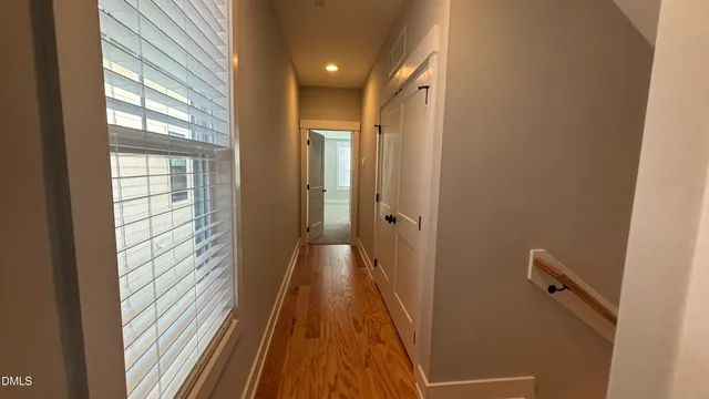 a view of a hallway with wooden floor and a bathroom