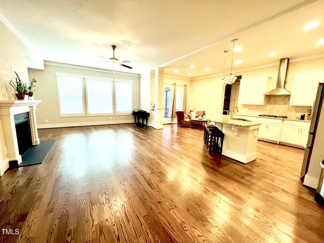 a living room with stainless steel appliances kitchen island granite countertop a sink a stove and white cabinets with wooden floor