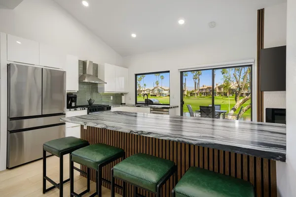 a kitchen with stainless steel appliances granite countertop a refrigerator a stove a sink a dining table and chairs with wooden floor