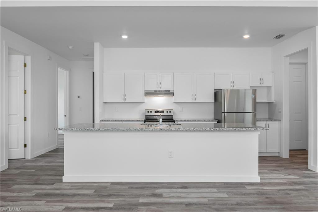 1515 Nelson Road North Cape Coral, FL 33993 - Photo 12 of 38 a large kitchen with stainless steel appliances granite countertop a stove a sink a refrigerator and white cabinets with wooden floor