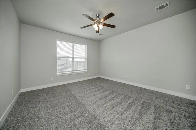 an empty room with ceiling fan and windows