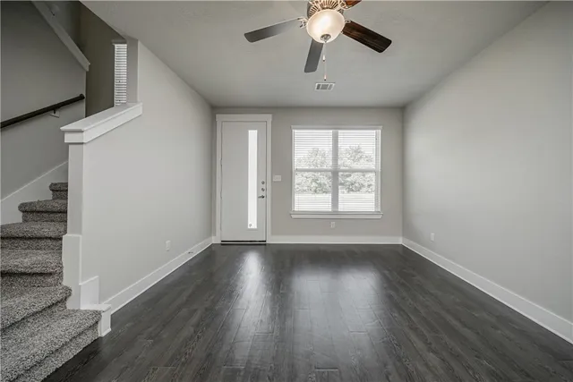 an empty room with wooden floor chandelier fan and windows