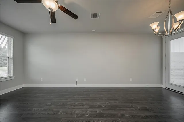 an empty room with wooden floor fan and windows