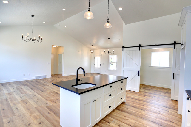 1257 North 1350th Street East Mapleton, UT 84664 - Photo 8 of 34 Vaulted ceilings with recessed lighting, wood-finish flooring, kitchen island with integrated sink, black countertops, and a sliding barn door