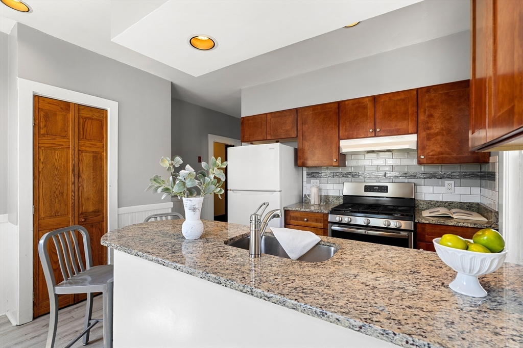 2 Thorndike Street, Unit 2 Arlington, MA 02474 - Photo 12 of 22 a kitchen with stainless steel appliances granite countertop a sink a stove a dining table and chairs with wooden floor