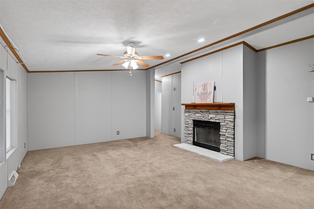 1202 Princeton Road Princeton, LA 71067 - Photo 7 of 32 Unfurnished living room featuring crown molding, ceiling fan, light carpet, a stone fireplace, and a decorative wall