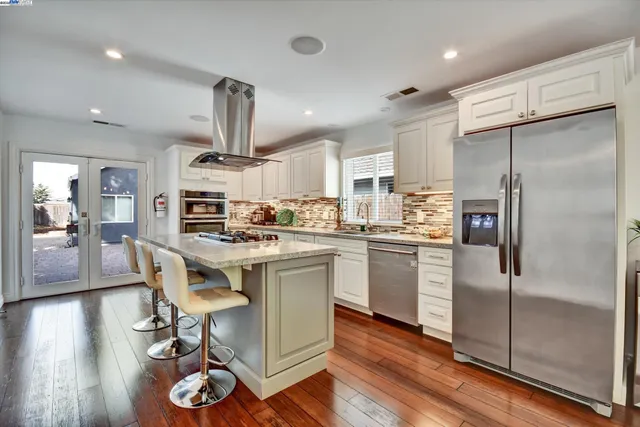 a kitchen with stainless steel appliances kitchen island granite countertop a refrigerator a stove a sink and a dining table with wooden floor