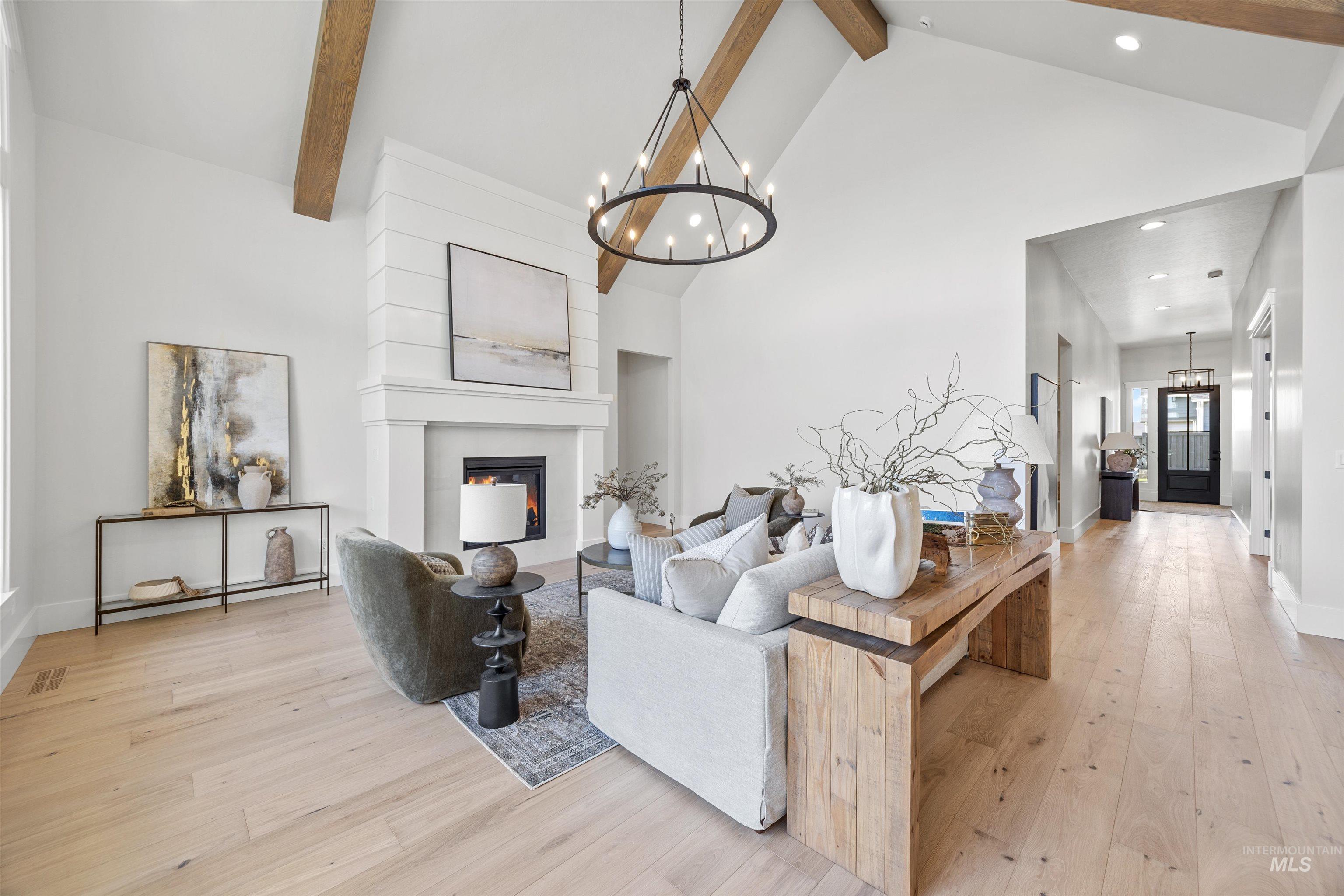 5940 South Pinpoint Way Meridian, ID 83642 - Photo 14 of 40 Vaulted ceilings with exposed wood beams, a fireplace with shiplap surround, wood-finish flooring, a contemporary chandelier, and recessed lighting