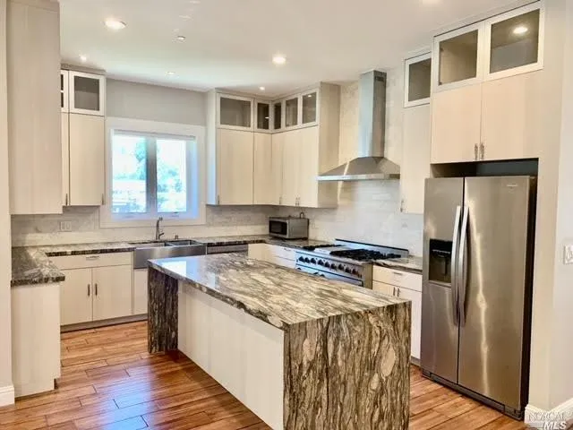 a kitchen with stainless steel appliances granite countertop a stove a refrigerator a sink dishwasher a refrigerator white cabinets and wooden floor next to a window