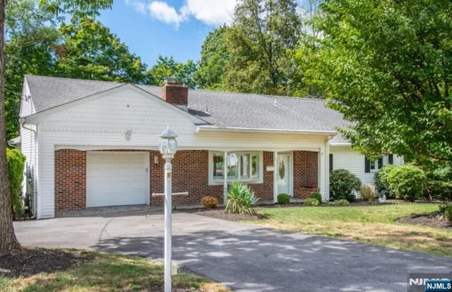 a view of a brick house with a yard plants and large tree