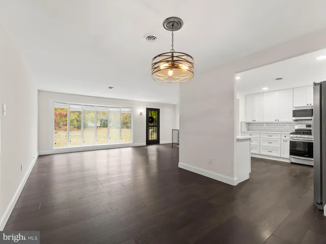 a view of an empty room with wooden floor and kitchen view