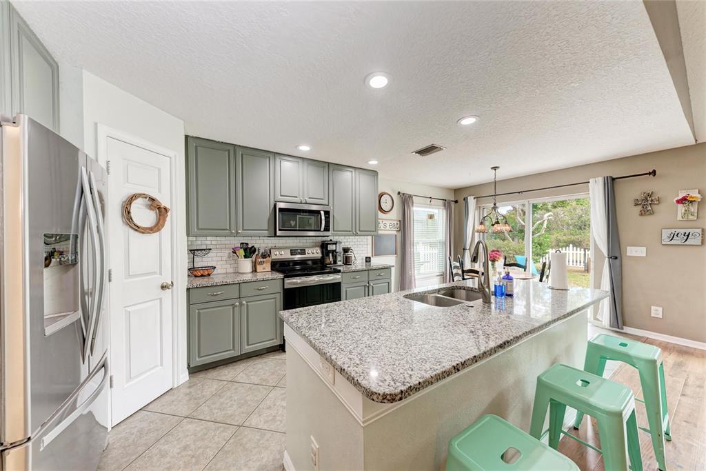 4608 Oliver Manor Drive Parrish, FL 34219 - Photo 9 of 45 a kitchen with kitchen island granite countertop a stove top oven a sink dishwasher a dining table and chairs with wooden floor