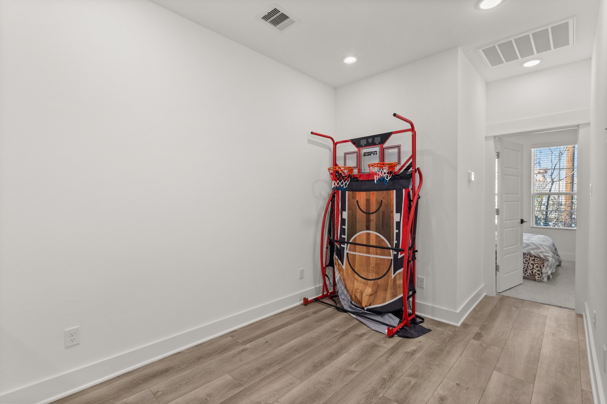 2928 Stevens Street Houston, TX 77026 - Photo 18 of 30 This room features a bright, minimalist space with light wood flooring and recessed lighting. It currently houses a mini basketball game setup. There's a doorway leading to a carpeted bedroom with ample natural light. Ideal for a playroom or home office.