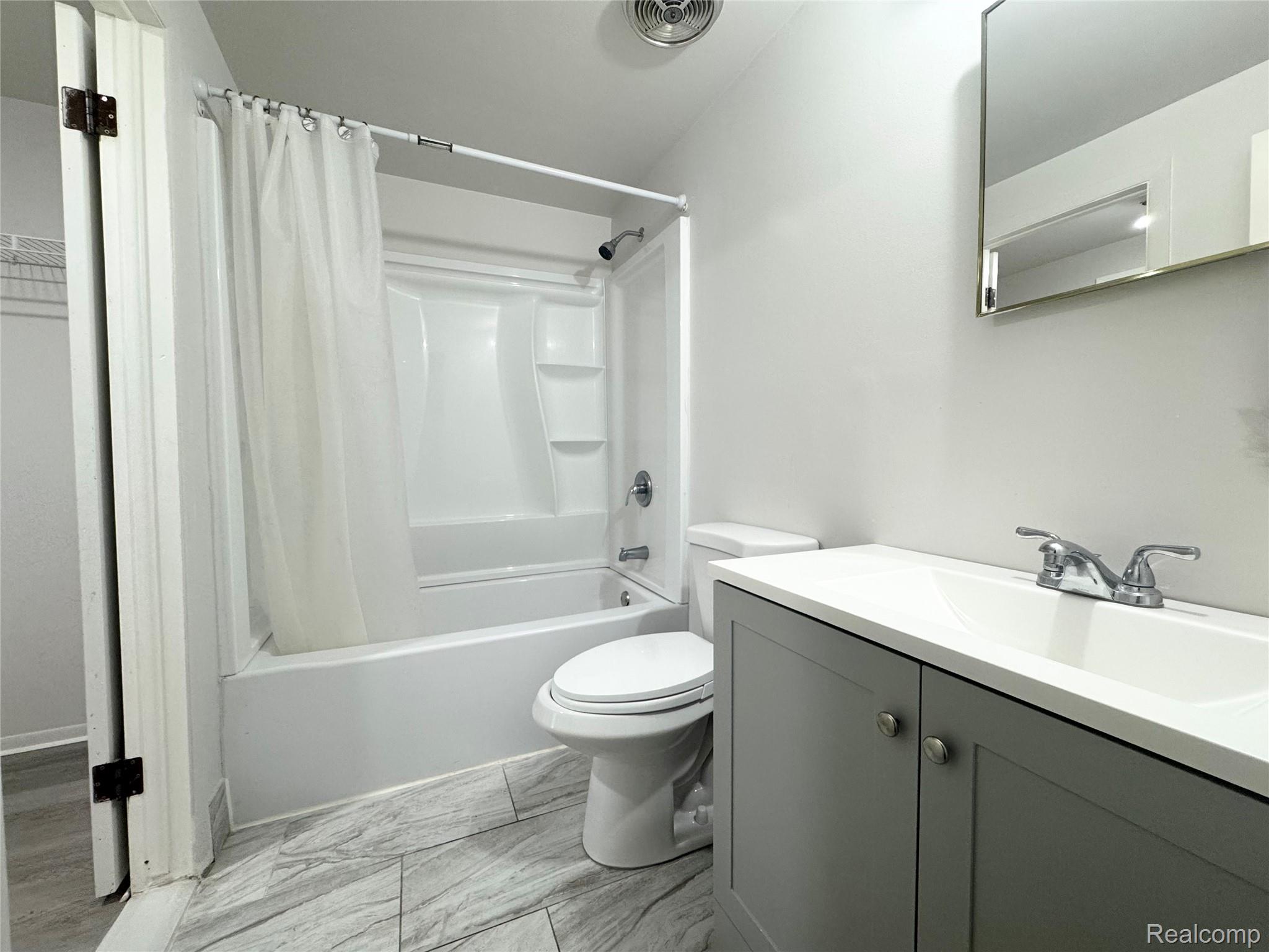 4386 15 Mile Road, Unit 64 Sterling Heights, MI 48310 - Photo 8 of 23 Bathroom featuring a white bathtub and shower combination, a white toilet, a gray vanity with a white countertop and integrated sink, and a mirrored medicine cabinet