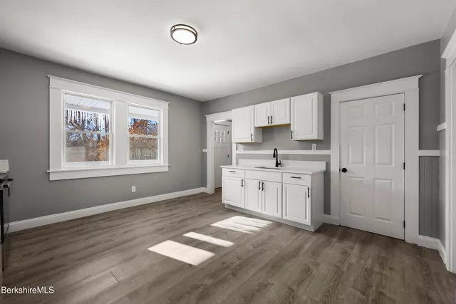 a kitchen with granite countertop a stove a sink and white cabinets with wooden floor