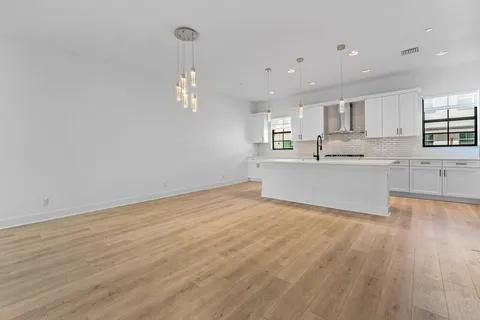 an empty room with wooden floor and kitchen view