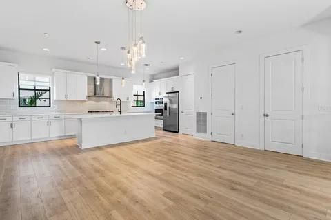 a view of a kitchen with kitchen island a sink wooden floor and stainless steel appliances