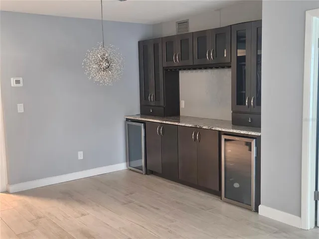 an empty room with chandelier fan and kitchen view