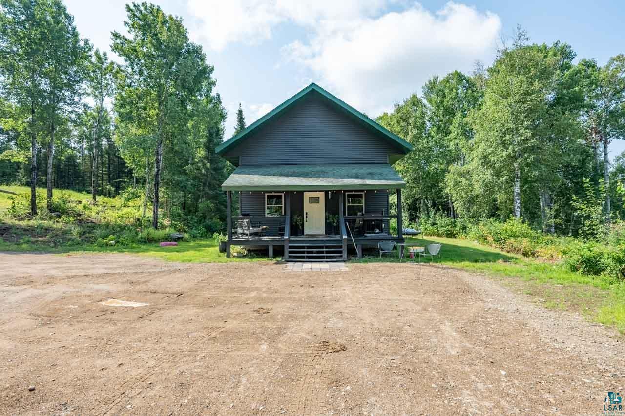 Siding exterior with a covered front porch, white entry door, and perimeter of mature trees