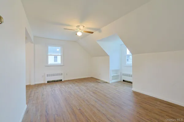 an empty room with wooden floor chandelier fan and windows
