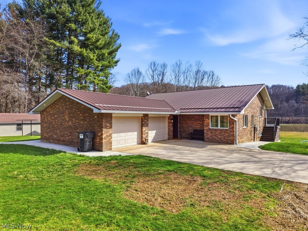 1430 Magnolia Road Southwest Dellroy, OH 44620 - Photo 2 of 50 Welcoming front exterior featuring a spacious driveway, attached 2-car garage, and a peaceful setting surrounded by mature trees.