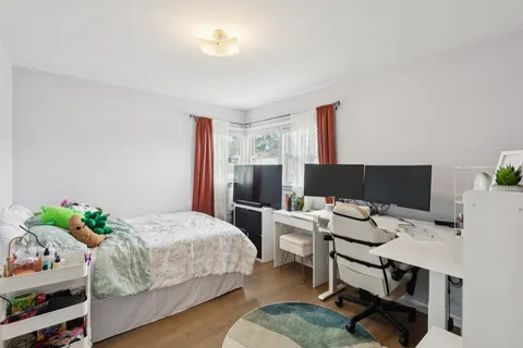 a bedroom with a bed and a computer on a desk next to a window