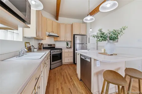 a kitchen with stainless steel appliances a stove a sink dishwasher a refrigerator white cabinets and wooden floor