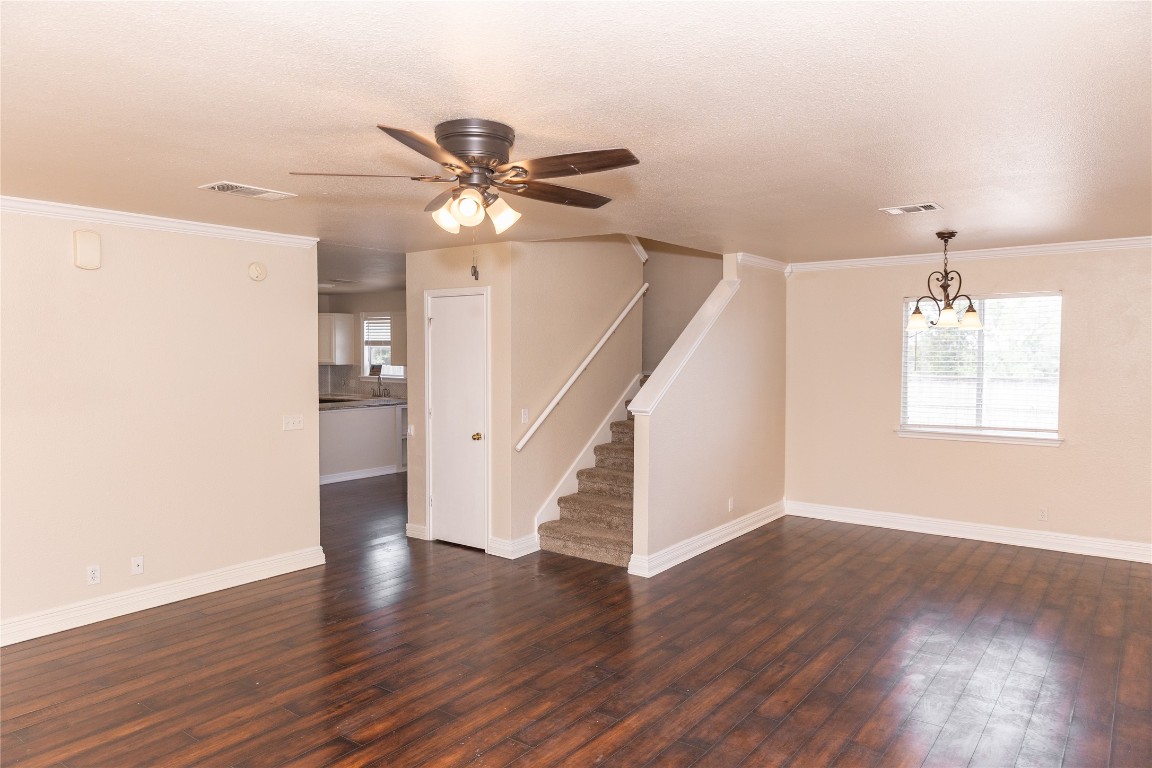 184 Unity Kyle, TX 78640 - Photo 28 of 33 Unfurnished living room featuring dark wood finished floors, ornamental molding, stairs, ceiling fan, and a chandelier