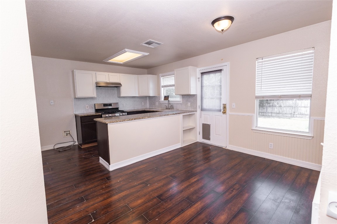 184 Unity Kyle, TX 78640 - Photo 5 of 33 Kitchen featuring white cabinets, dark wood-type flooring, tasteful backsplash, stainless steel gas range oven, and a peninsula