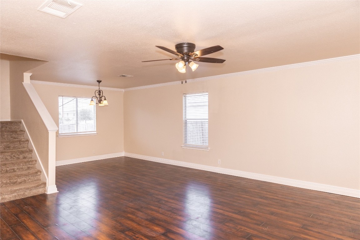 184 Unity Kyle, TX 78640 - Photo 9 of 33 Unfurnished room with stairs, dark wood-type flooring, ornamental molding, a ceiling fan, and a chandelier