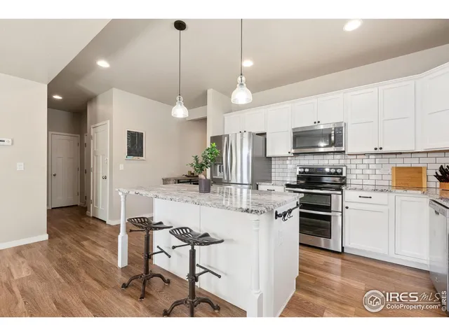 a kitchen with stainless steel appliances kitchen island granite countertop a refrigerator a stove a sink a dining table and chairs with wooden floor