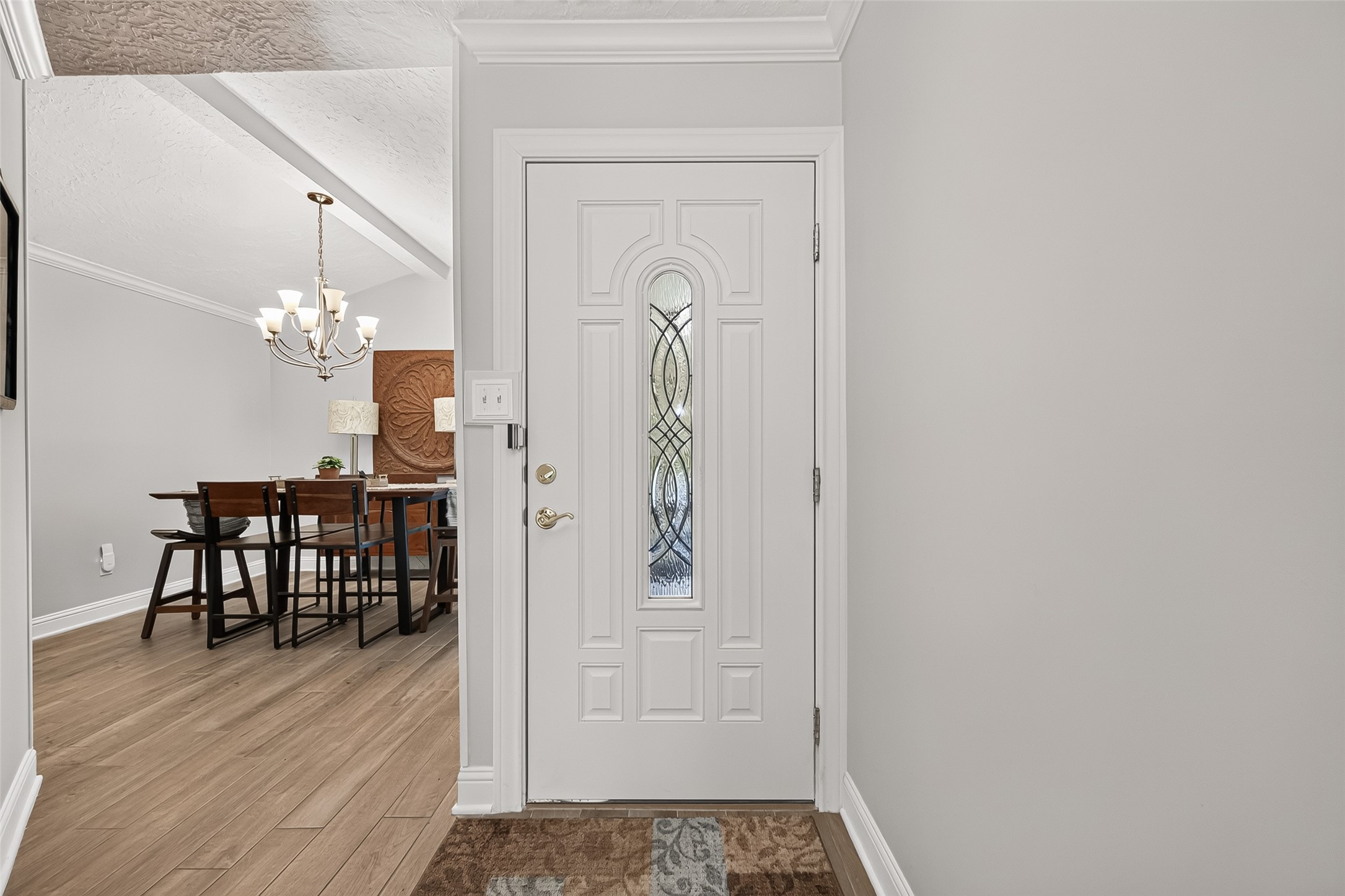 24719 Wilderness Road Spring, TX 77380 - Photo 6 of 42 This photo shows a welcoming entryway with a white door featuring decorative glass. Adjacent is a dining area with a chandelier, ceramic tile flooring, and neutral walls, creating a warm and inviting atmosphere.