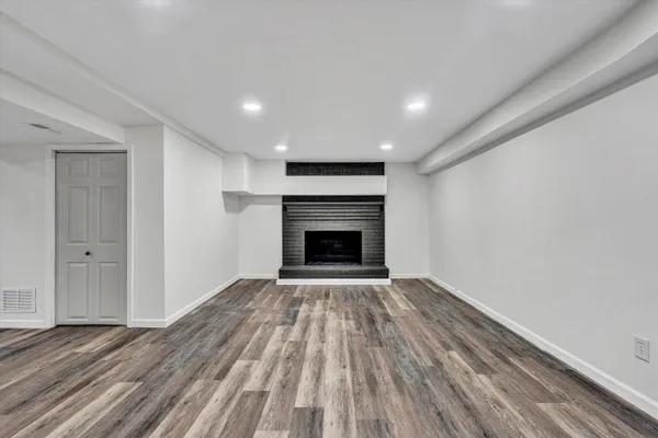 a view of an empty room with wooden floor fireplace and a window