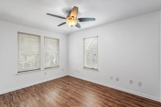 an empty room with wooden floor fan and windows