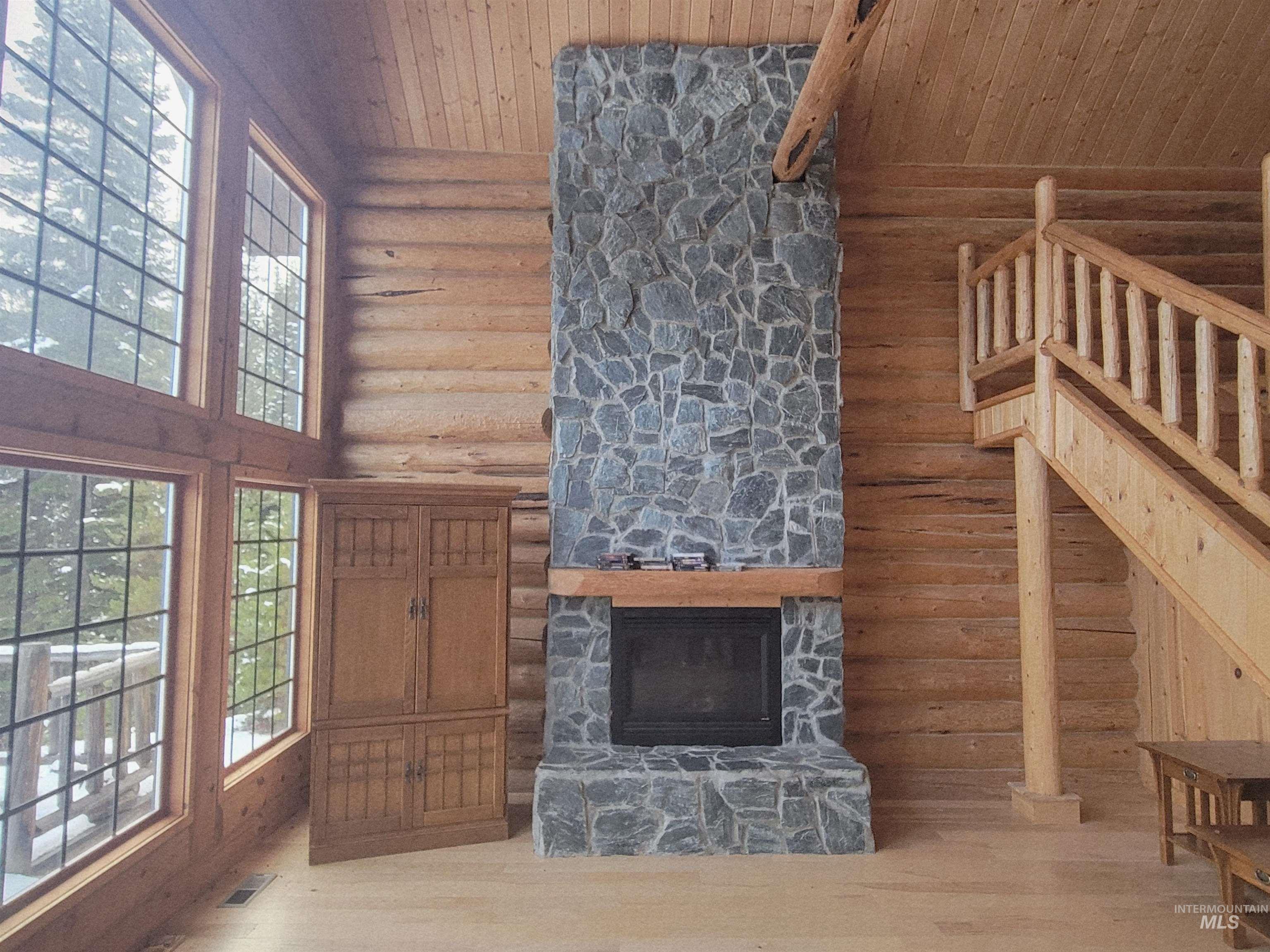 129 Copperhead Road Elk City, ID 83525 - Photo 12 of 28 Unfurnished living room featuring log walls, high vaulted ceiling, a stone fireplace, wood ceiling, and healthy amount of natural light