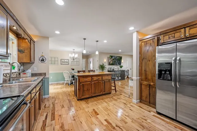 a kitchen with stainless steel appliances granite countertop a refrigerator a sink dishwasher a oven and a dining table with wooden floor