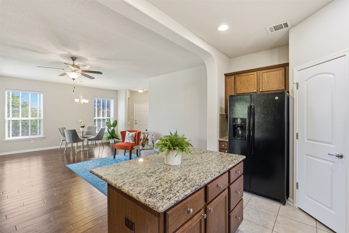 3451 Mayfield Ranch Boulevard, Unit 369 Round Rock, TX 78681 - Photo 29 of 29 Kitchen with black refrigerator with ice dispenser, brown cabinets, a center island, light stone counters, and open floor plan