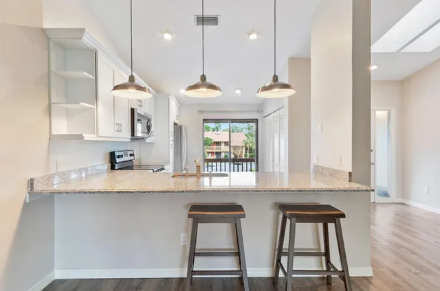 a kitchen with kitchen island granite countertop a stove a sink a dining table and chairs with wooden floor