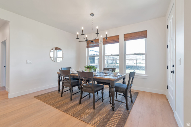 1820 West Farmhouse Flats Road Peoa, UT 84061 - Photo 18 of 79 Dining area featuring a modern black chandelier, three windows with natural woven shades, light wood-finish flooring, and a white paneled door with a black handle