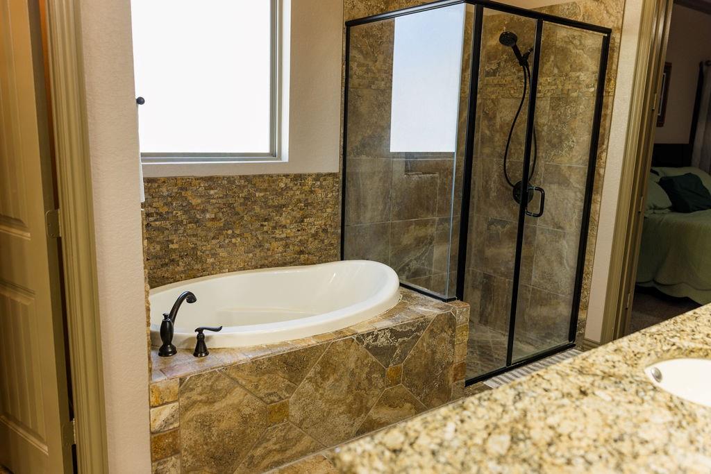123 Cactus Drive Decatur, TX 76234 - Photo 18 of 30 Soaking tub with bronze fixtures, glass-enclosed shower, stone tile surround, and a window for natural light