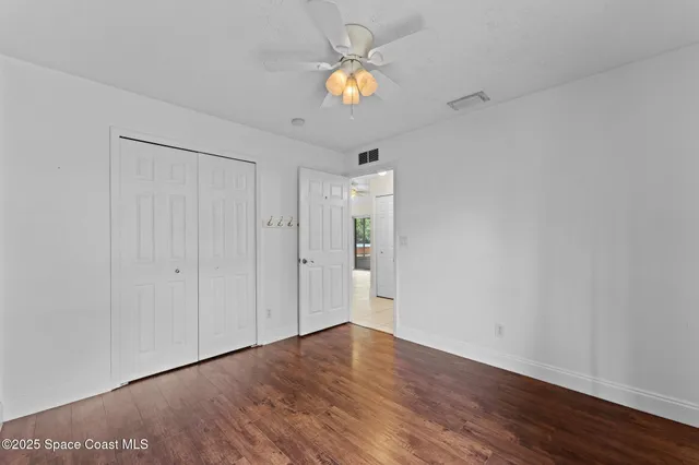 a view of an empty room and wooden floor and a chandelier fan