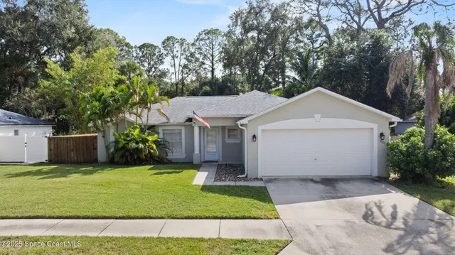 a view of a white house with a yard plants and large tree