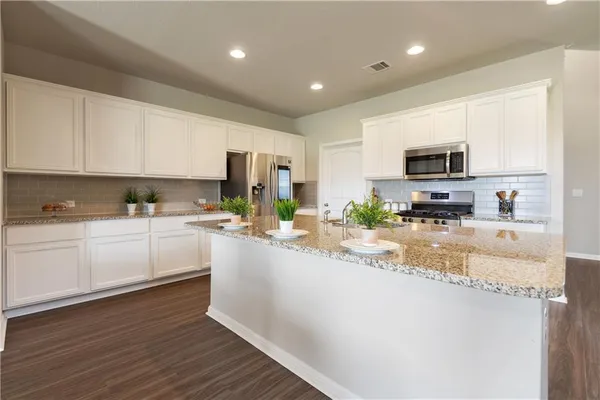 a kitchen with granite countertop a refrigerator a sink dishwasher a stove and white cabinets with wooden floor