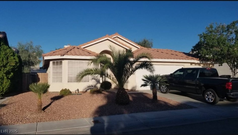View of front facade with a garage, stucco siding, a tile roof, and concrete driveway